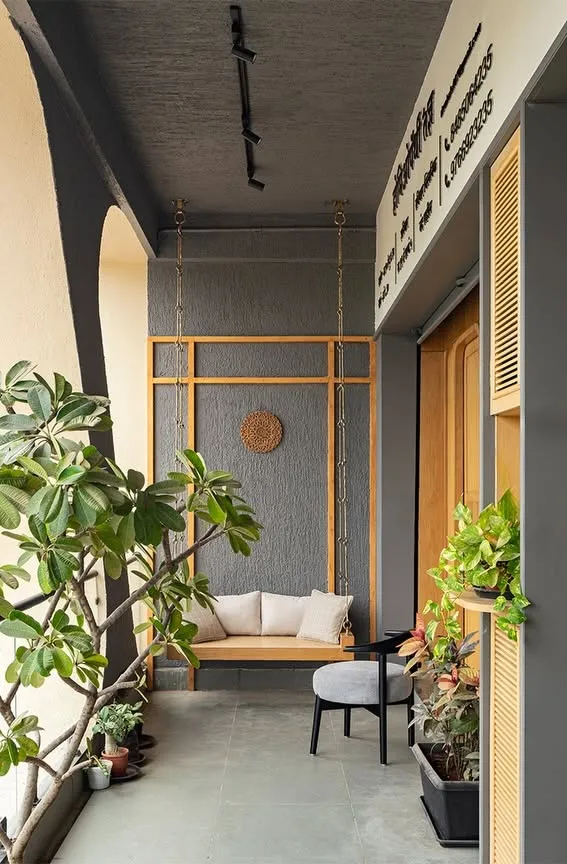 A balcony with a wooden swing, plants and a grey textured wall