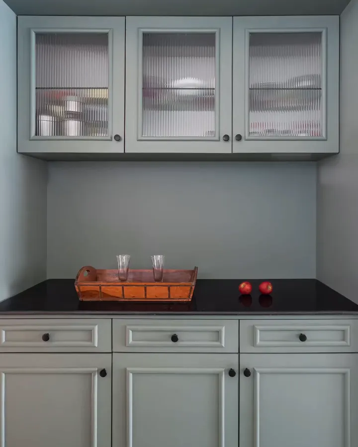 Sage green kitchen cabinets with fluted glass shutters and a black granite counter
