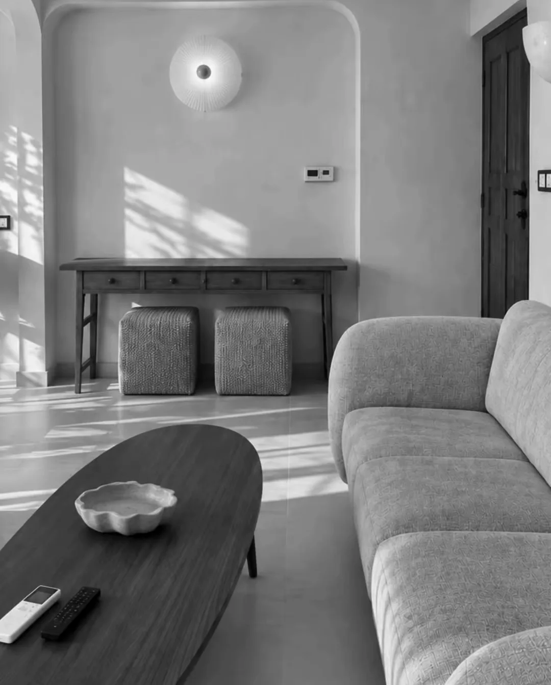 The finished living room: a grey sofa, an oval coffee table and a console in an arched niche, in afternoon sun